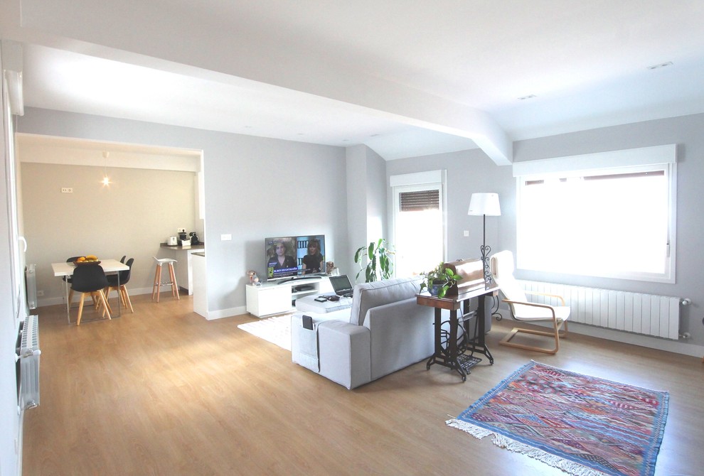 Modelo de salón abierto contemporáneo grande con paredes grises, suelo laminado, televisor independiente y suelo marrón
