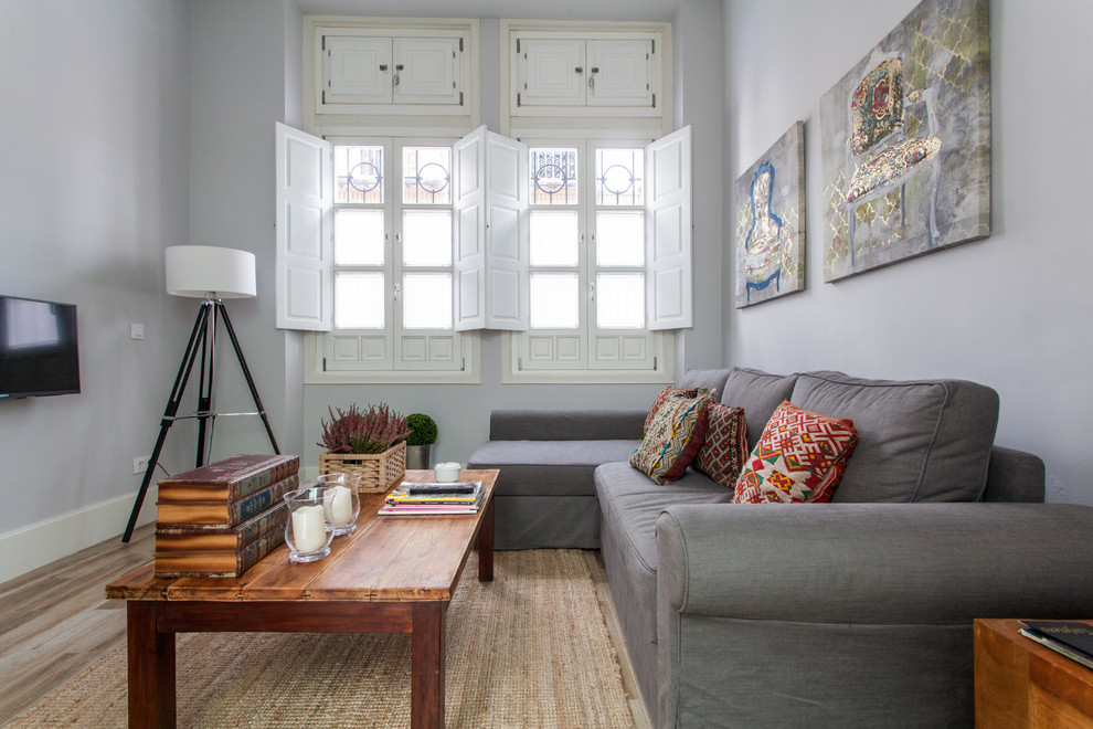 Diseño de salón para visitas abierto moderno de tamaño medio sin chimenea con paredes grises, suelo de madera en tonos medios y televisor colgado en la pared