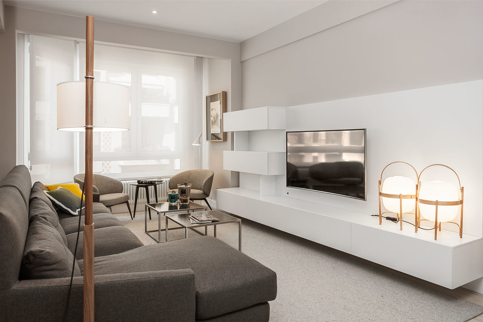 Imagen de salón para visitas abierto contemporáneo de tamaño medio sin chimenea con paredes grises, suelo de madera clara y televisor retractable