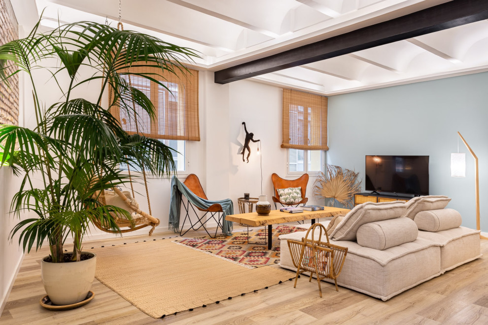 Diseño de salón abierto exótico sin chimenea con paredes azules, suelo de madera clara, televisor independiente, suelo beige y vigas vistas