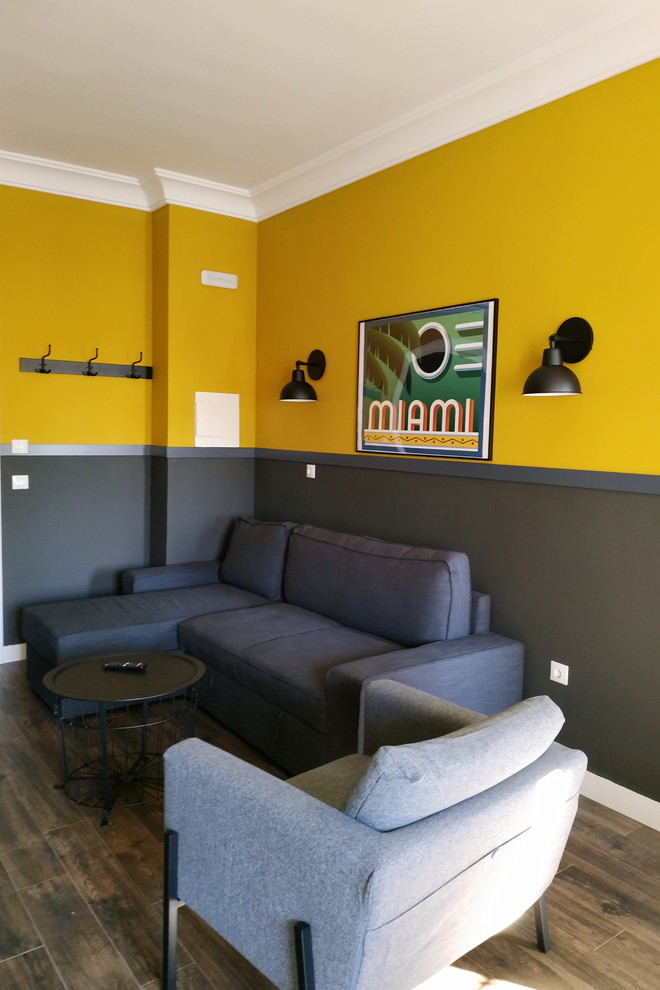 Cette image montre un petit salon ouvert avec un mur jaune, un sol en carrelage de céramique, un téléviseur fixé au mur et un sol marron.