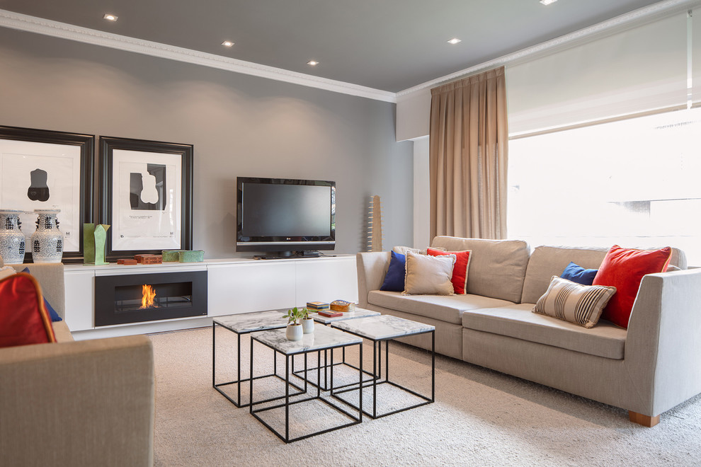This is an example of a medium sized bohemian open plan living room in Bilbao with grey walls, carpet, a ribbon fireplace, a metal fireplace surround, a freestanding tv and grey floors.