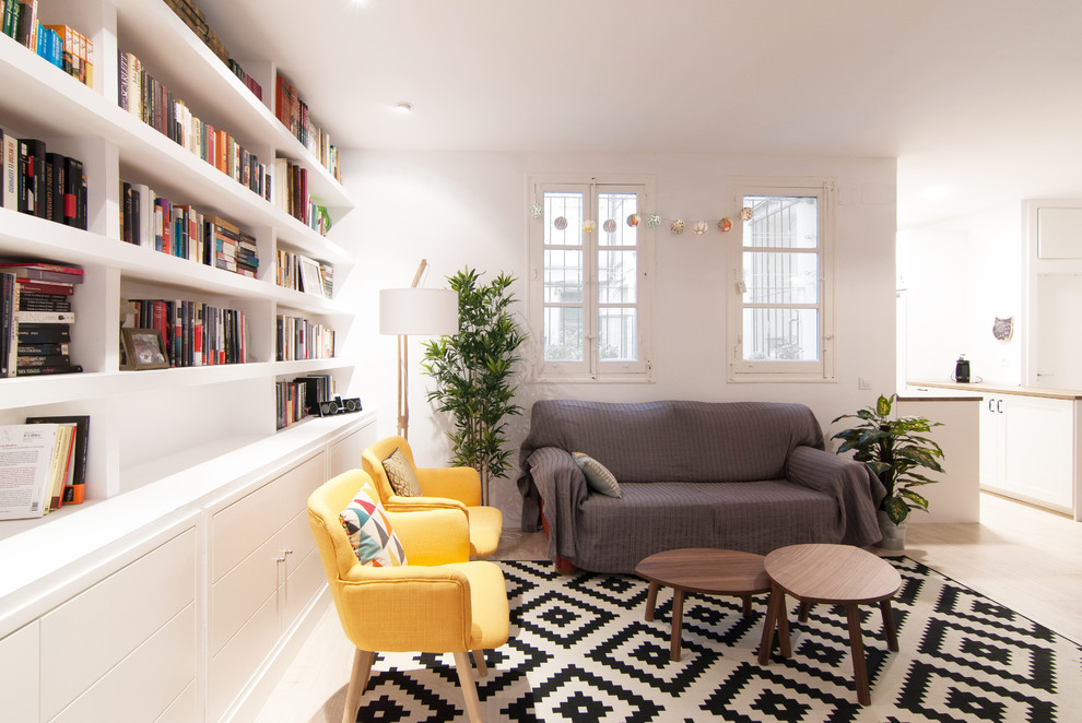 Ejemplo de biblioteca en casa abierta escandinava de tamaño medio sin chimenea con paredes blancas, suelo de madera clara, pared multimedia y suelo beige