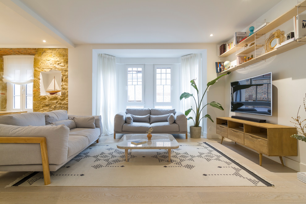 Modelo de salón escandinavo con paredes blancas, suelo de madera clara, televisor colgado en la pared, suelo beige y piedra