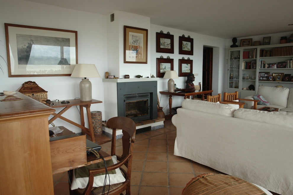 Mediterranes Wohnzimmer mit weißer Wandfarbe, Terrakottaboden, Kaminumrandung aus Metall und Kaminofen in Sonstige