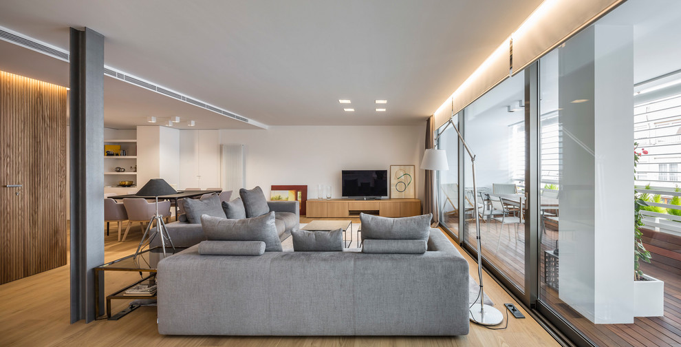 Modelo de salón abierto actual de tamaño medio con paredes blancas, suelo de madera en tonos medios, televisor independiente y suelo marrón
