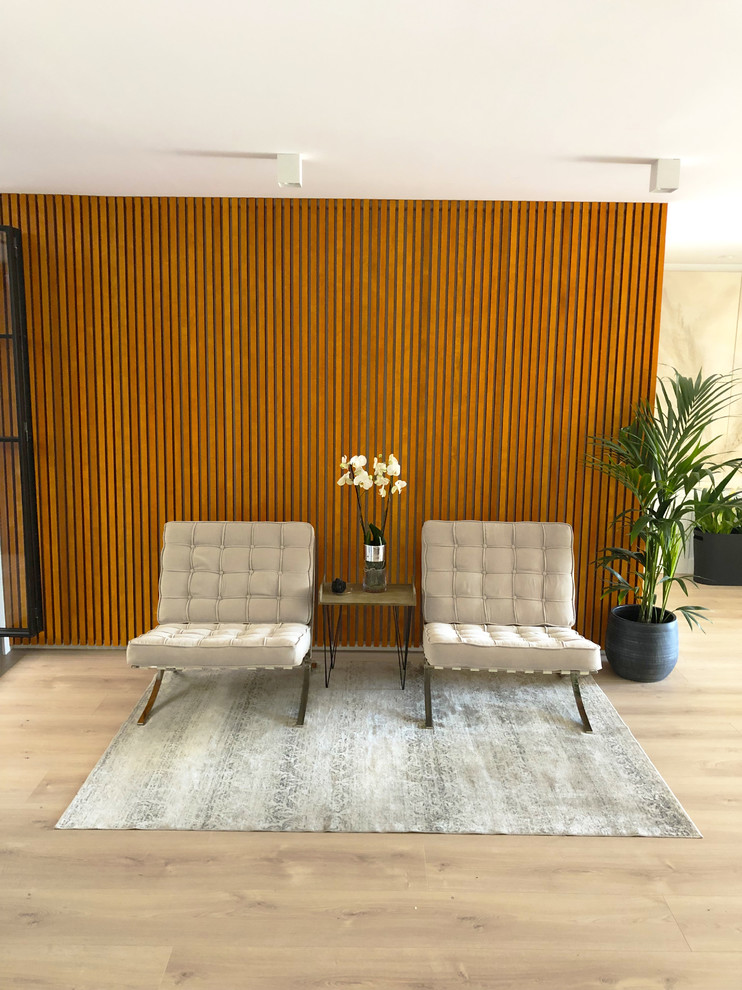 Modelo de salón abierto actual grande con paredes blancas, suelo de madera en tonos medios, televisor colgado en la pared y suelo marrón