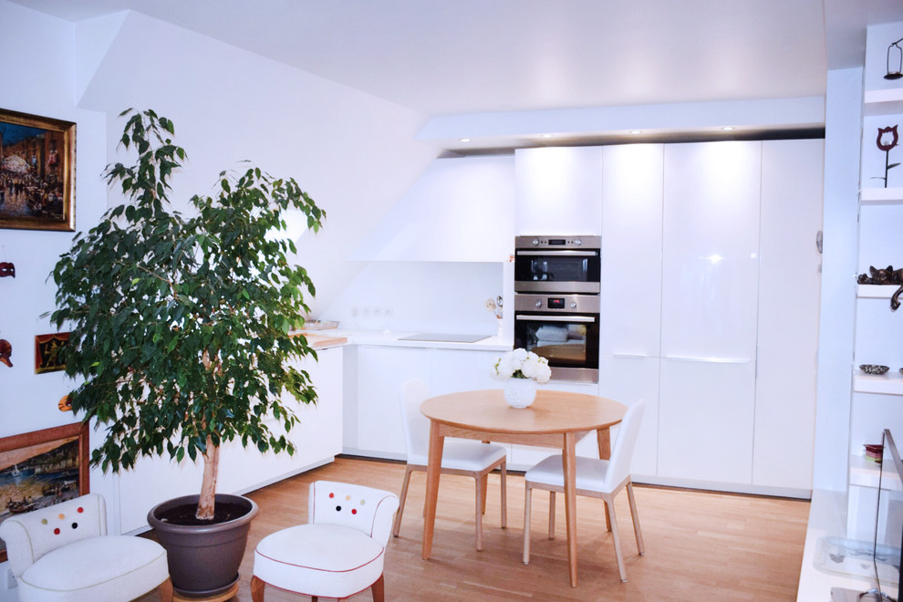 Foto di una piccola cucina contemporanea con parquet chiaro, pavimento marrone, ante bianche, paraspruzzi bianco, elettrodomestici da incasso, nessuna isola e top bianco