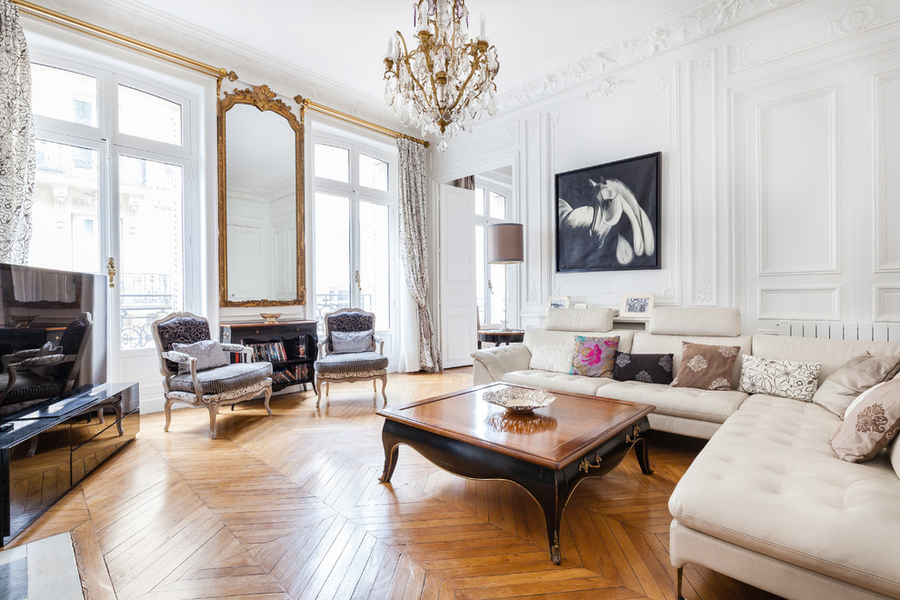 Inspiration for a traditional formal living room in Paris with white walls, medium hardwood flooring, a freestanding tv, brown floors and feature lighting.
