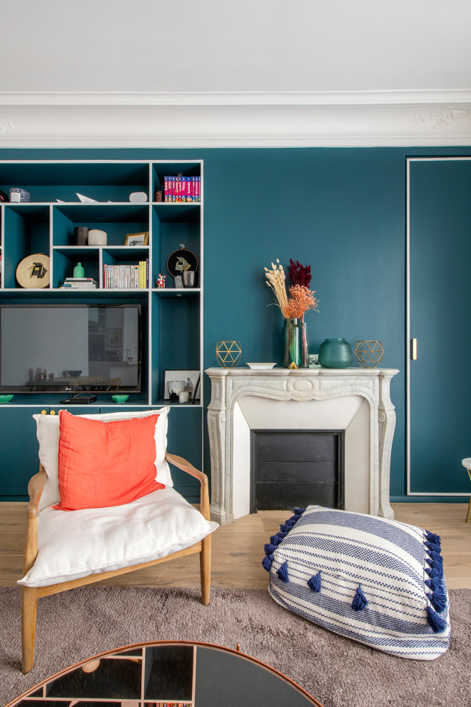 パリにあるお手頃価格の中くらいなコンテンポラリースタイルのおしゃれなLDK (ライブラリー、青い壁、淡色無垢フローリング、標準型暖炉、石材の暖炉まわり、据え置き型テレビ、ベージュの床) の写真