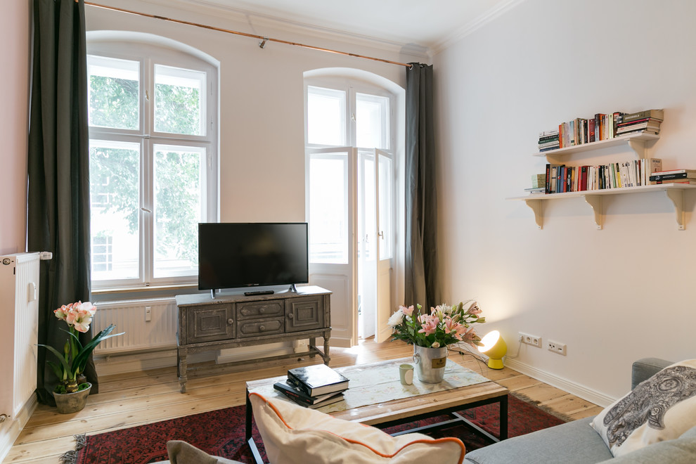 This is an example of a medium sized industrial formal enclosed living room in Berlin with white walls, medium hardwood flooring, no fireplace, a freestanding tv and brown floors.