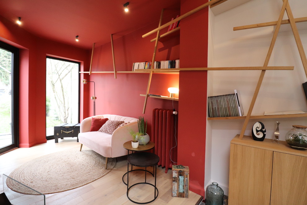 На фото: открытая гостиная комната среднего размера в современном стиле с с книжными шкафами и полками, красными стенами и светлым паркетным полом без телевизора с