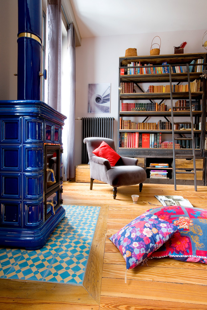 Exemple d'un salon éclectique avec un mur rose, un sol en bois brun, un manteau de cheminée en carrelage, une bibliothèque ou un coin lecture et un poêle à bois.