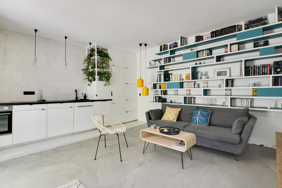 На фото: открытая гостиная комната среднего размера в скандинавском стиле с с книжными шкафами и полками, белыми стенами, бетонным полом, серым полом и скрытым телевизором без камина с