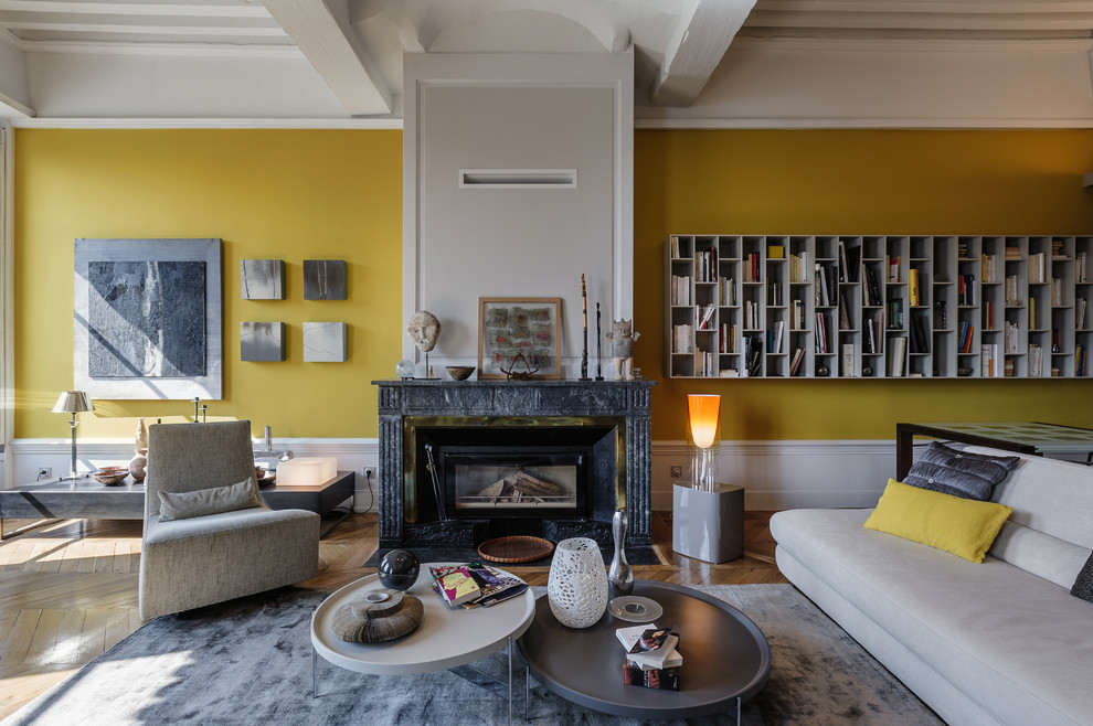 Cette image montre un grand salon gris et jaune bohème ouvert avec une salle de réception, un mur jaune, un sol en bois brun, une cheminée standard, un manteau de cheminée en pierre, aucun téléviseur et éclairage.