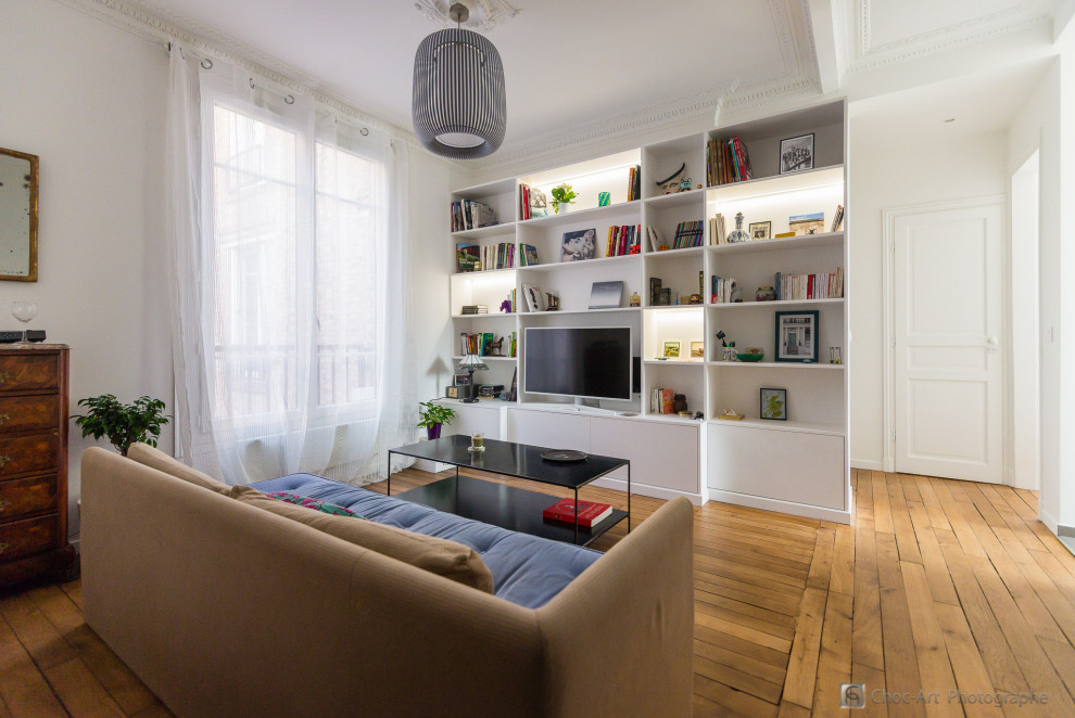Пример оригинального дизайна: маленькая открытая гостиная комната в современном стиле с с книжными шкафами и полками, белыми стенами, светлым паркетным полом, отдельно стоящим телевизором и коричневым полом без камина для на участке и в саду