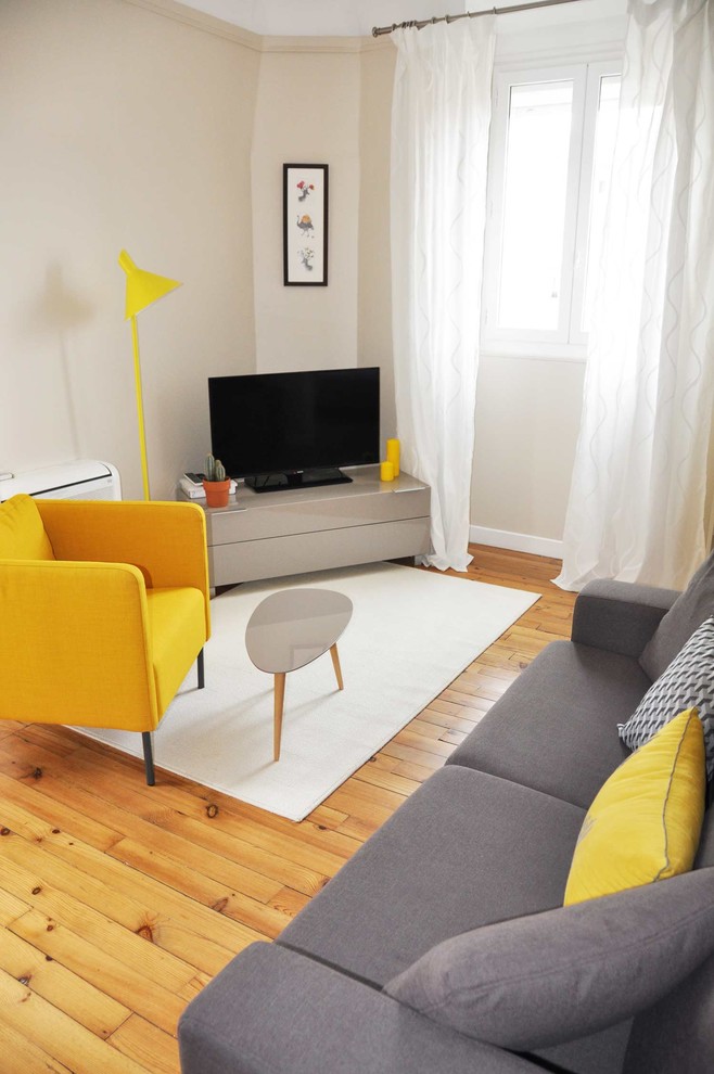 Medium sized contemporary grey and yellow enclosed living room in Paris with beige walls, medium hardwood flooring, no fireplace and a freestanding tv.