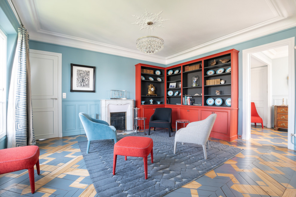 Стильный дизайн: большая изолированная гостиная комната в стиле неоклассика (современная классика) с с книжными шкафами и полками, синими стенами, деревянным полом, стандартным камином, фасадом камина из камня, разноцветным полом и панелями на стенах - последний тренд