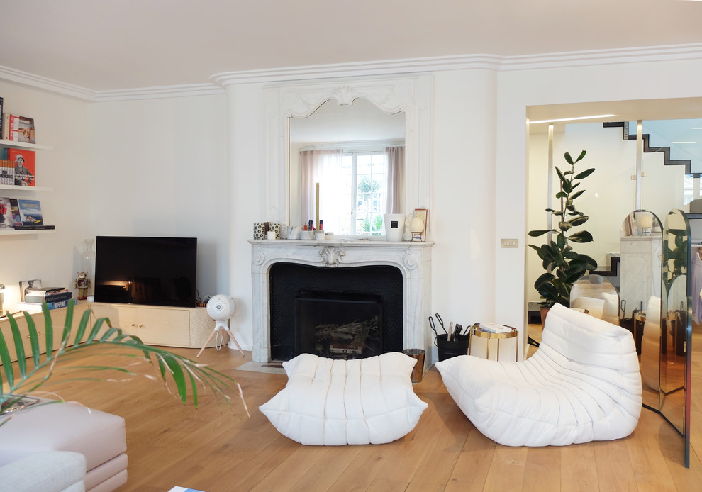 This is an example of a large contemporary enclosed living room in Paris with a reading nook, white walls, light hardwood flooring, a standard fireplace, a stone fireplace surround, a freestanding tv and brown floors.