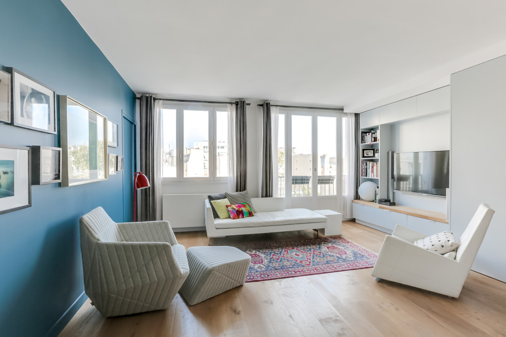 This is an example of a medium sized contemporary open plan living room in Paris with blue walls, light hardwood flooring, no fireplace, a wall mounted tv, a reading nook and feature lighting.
