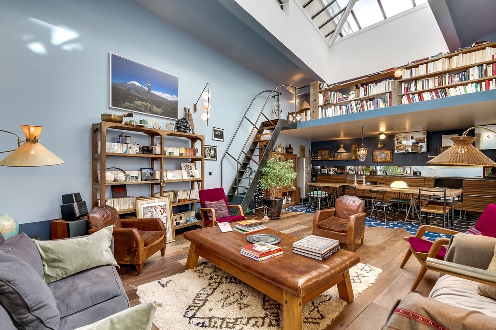 Modelo de biblioteca en casa abierta bohemia grande sin chimenea y televisor con paredes azules y suelo de madera en tonos medios