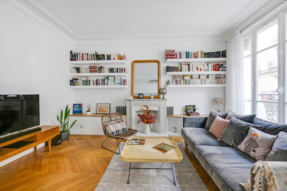 Large scandi open plan living room in Paris with a reading nook, white walls, a standard fireplace, a stone fireplace surround, a freestanding tv, medium hardwood flooring and brown floors.