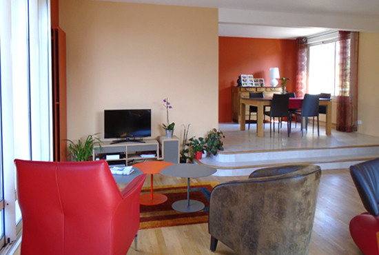 Foto de salón abierto contemporáneo de tamaño medio con parades naranjas, suelo de madera oscura, chimenea de doble cara y televisor independiente