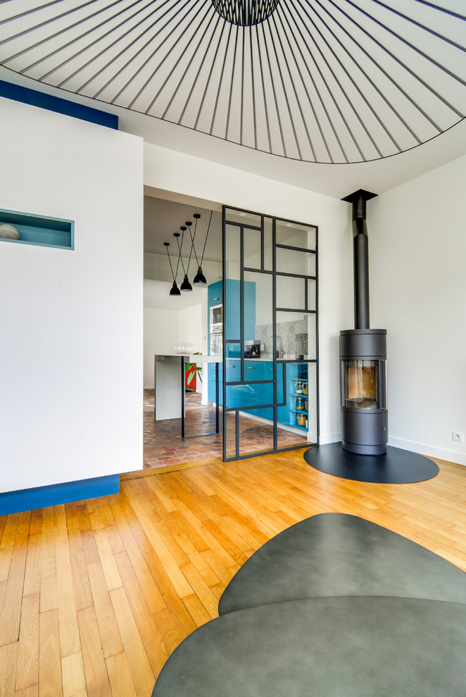 Mittelgroßes, Offenes Modernes Wohnzimmer mit weißer Wandfarbe, dunklem Holzboden, Kaminofen, Kaminumrandung aus Metall, freistehendem TV und braunem Boden in Paris