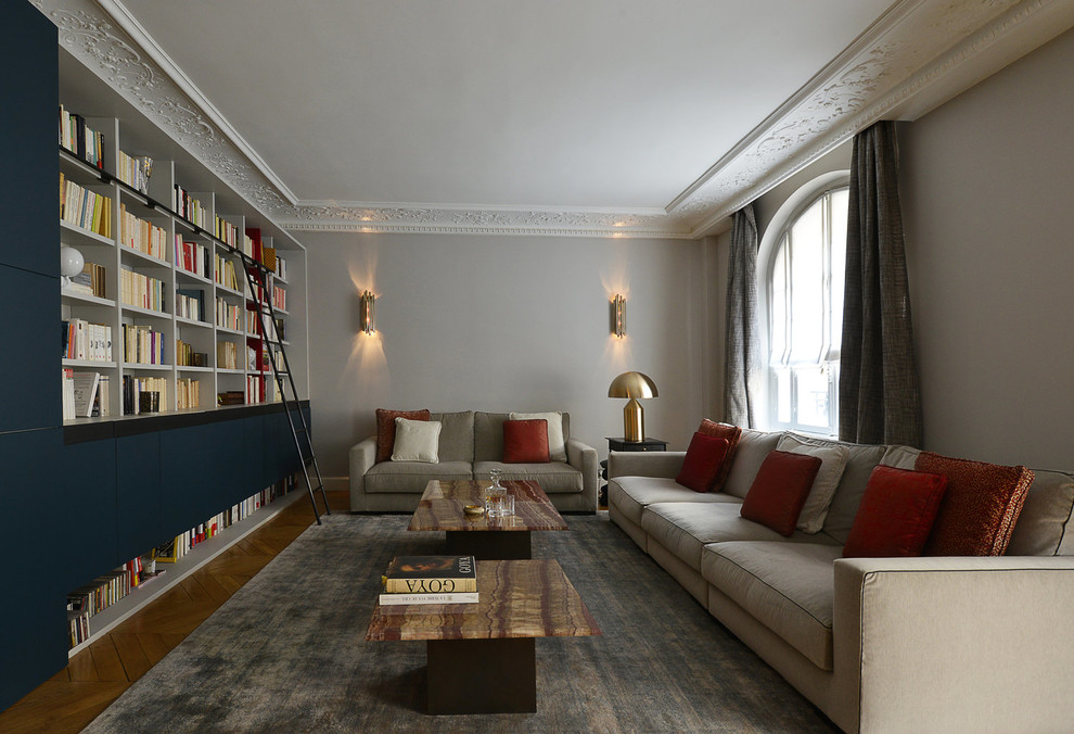 Große Moderne Bibliothek mit blauer Wandfarbe, braunem Holzboden und verstecktem TV in Paris