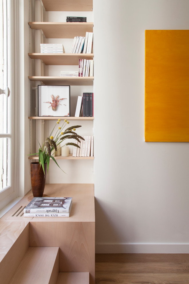 Aménagement d'un salon scandinave avec une bibliothèque ou un coin lecture, un mur blanc, parquet clair et un sol beige.