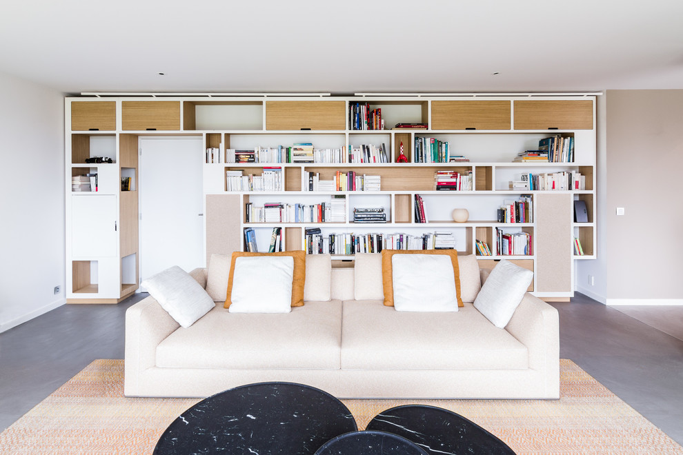 Cette photo montre un grand salon tendance fermé avec une bibliothèque ou un coin lecture, un mur beige, sol en béton ciré et un sol gris.