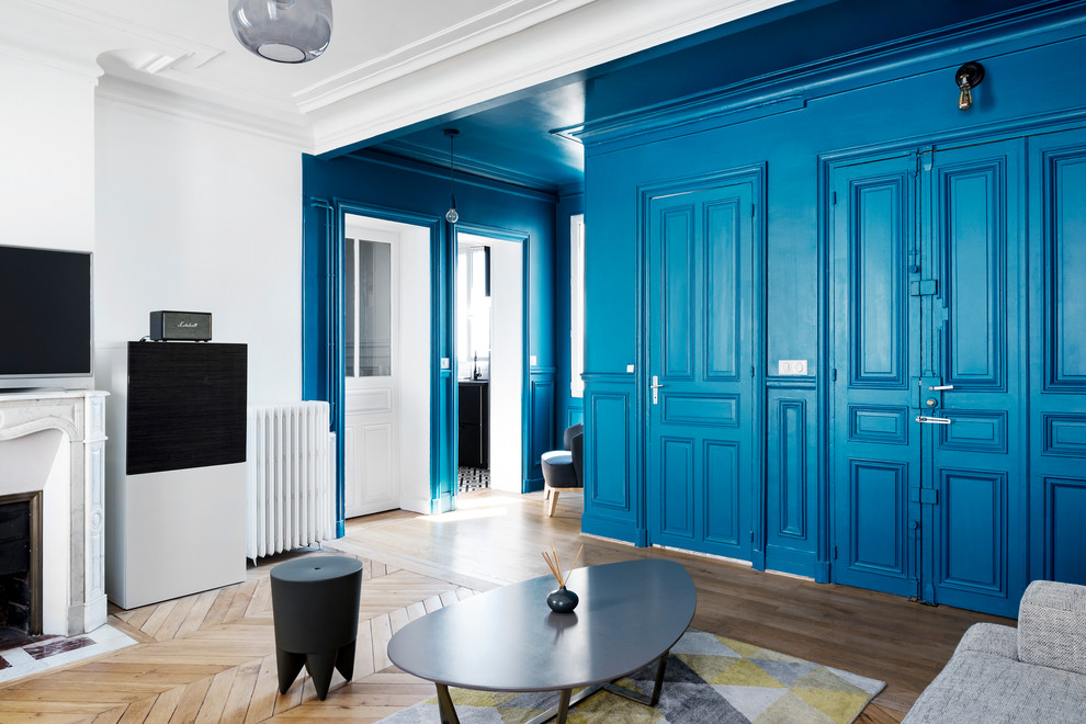 На фото: парадная, открытая гостиная комната среднего размера в стиле ретро с синими стенами, светлым паркетным полом, стандартным камином, фасадом камина из камня, отдельно стоящим телевизором и коричневым полом с