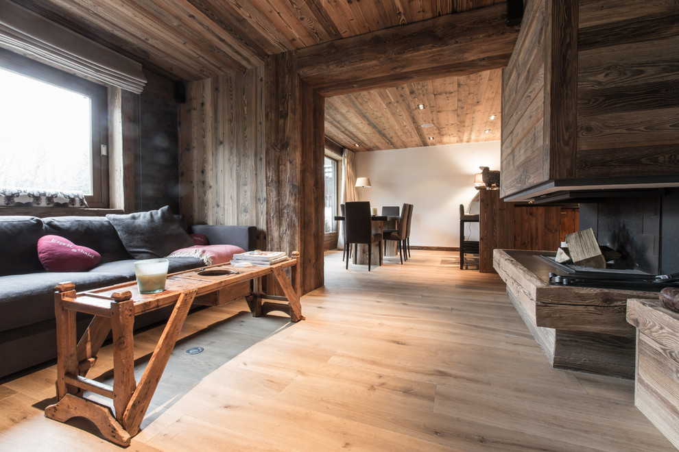 Diseño de salón abierto rústico grande sin televisor con paredes marrones, suelo de madera clara, todas las chimeneas y marco de chimenea de madera