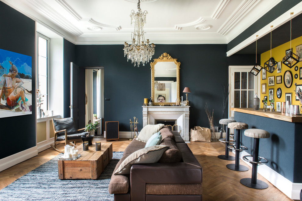 Idée de décoration pour un grand salon bohème ouvert avec un bar de salon, une cheminée standard, un manteau de cheminée en pierre, un téléviseur dissimulé, un sol marron, un mur bleu et un sol en bois brun.