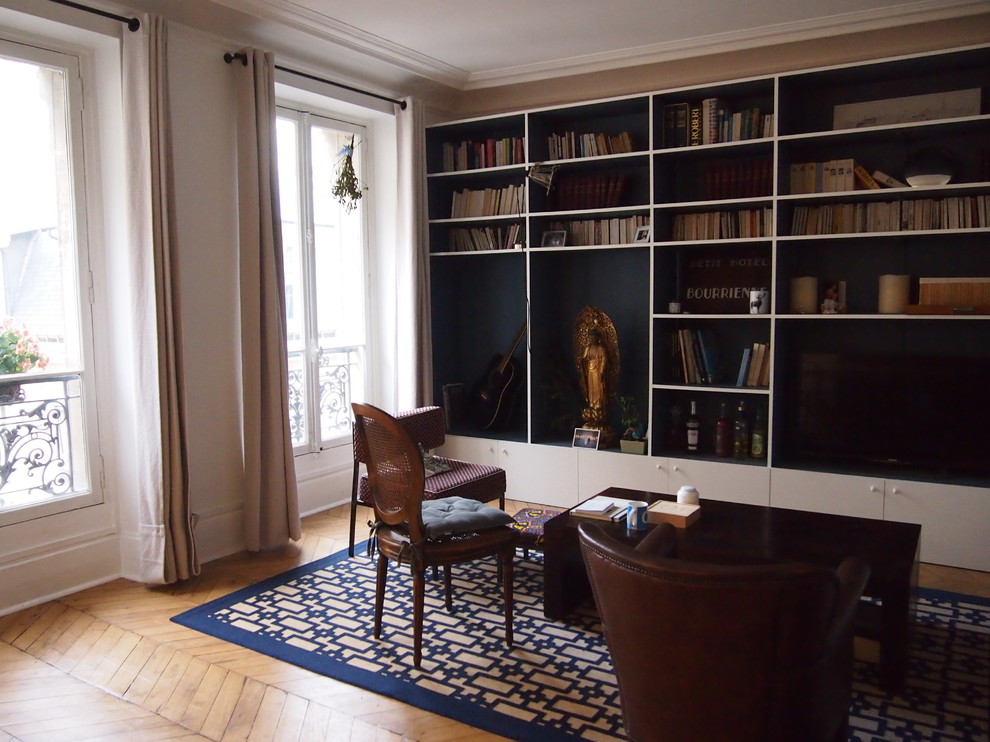 Cette image montre un salon bohème de taille moyenne et ouvert avec une bibliothèque ou un coin lecture, un mur bleu, parquet clair, aucune cheminée, un téléviseur fixé au mur et un sol beige.