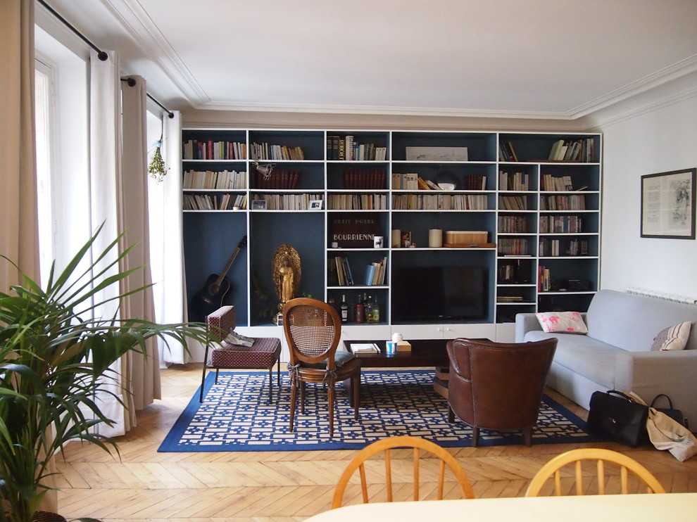 Idée de décoration pour un salon bohème de taille moyenne et ouvert avec une bibliothèque ou un coin lecture, un mur bleu, parquet clair, aucune cheminée, un téléviseur fixé au mur et un sol beige.