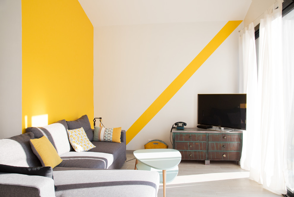 Imagen de salón abierto actual de tamaño medio sin chimenea con paredes amarillas, suelo de baldosas de cerámica, televisor independiente y suelo beige