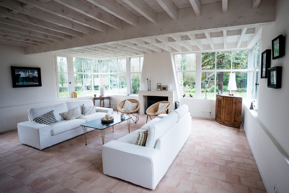 На фото: гостиная комната в морском стиле с белыми стенами, полом из терракотовой плитки, стандартным камином, фасадом камина из камня и розовым полом
