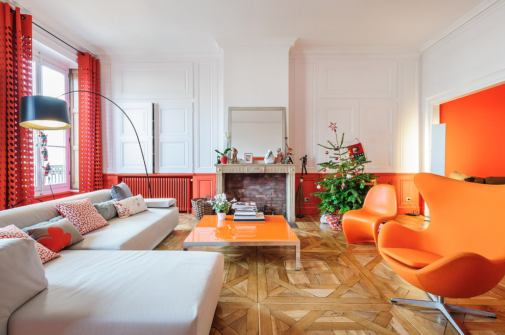 Repräsentatives, Abgetrenntes, Großes, Fernseherloses Modernes Wohnzimmer mit oranger Wandfarbe, hellem Holzboden und Kamin in Lyon