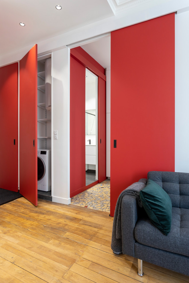 Bild på ett litet funkis allrum med öppen planlösning, med röda väggar, ljust trägolv, en standard öppen spis, en spiselkrans i trä, en dold TV och beiget golv
