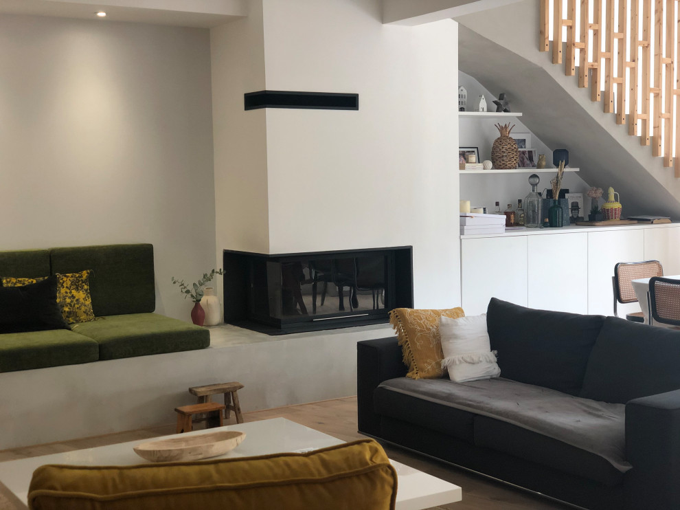 Example of a large eclectic open concept light wood floor, beige floor and exposed beam living room design in Toulouse with white walls, a standard fireplace and a plaster fireplace