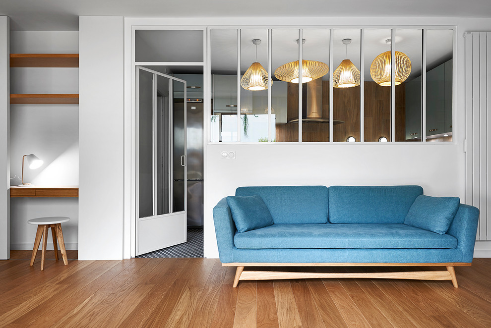 На фото: открытая гостиная комната среднего размера в скандинавском стиле с белыми стенами, паркетным полом среднего тона и синим диваном без камина
