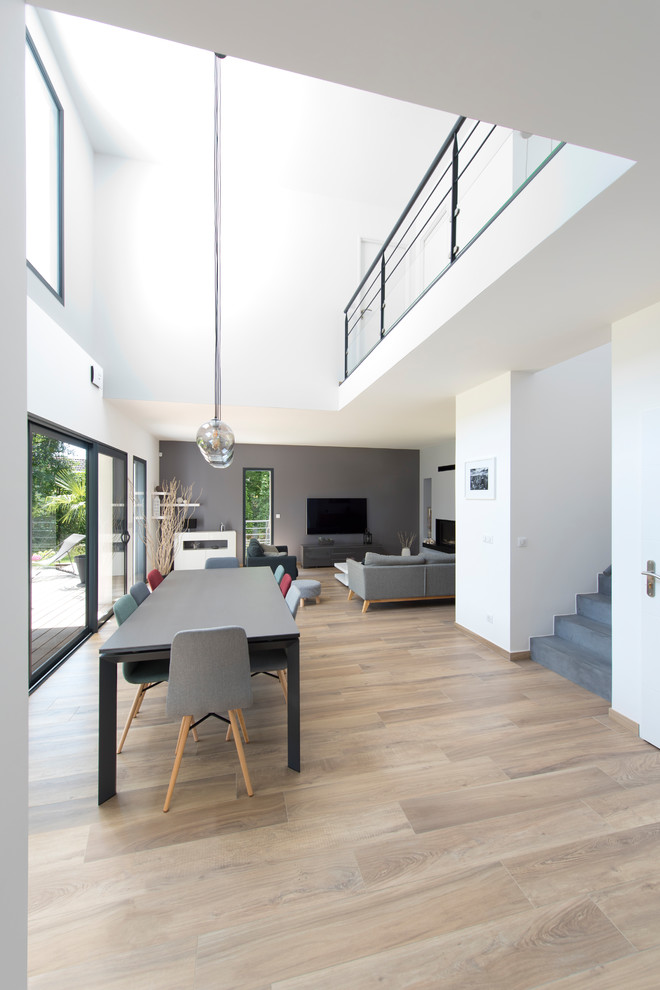 This is an example of a large contemporary open plan living room in Paris with white walls, light hardwood flooring, a freestanding tv and brown floors.
