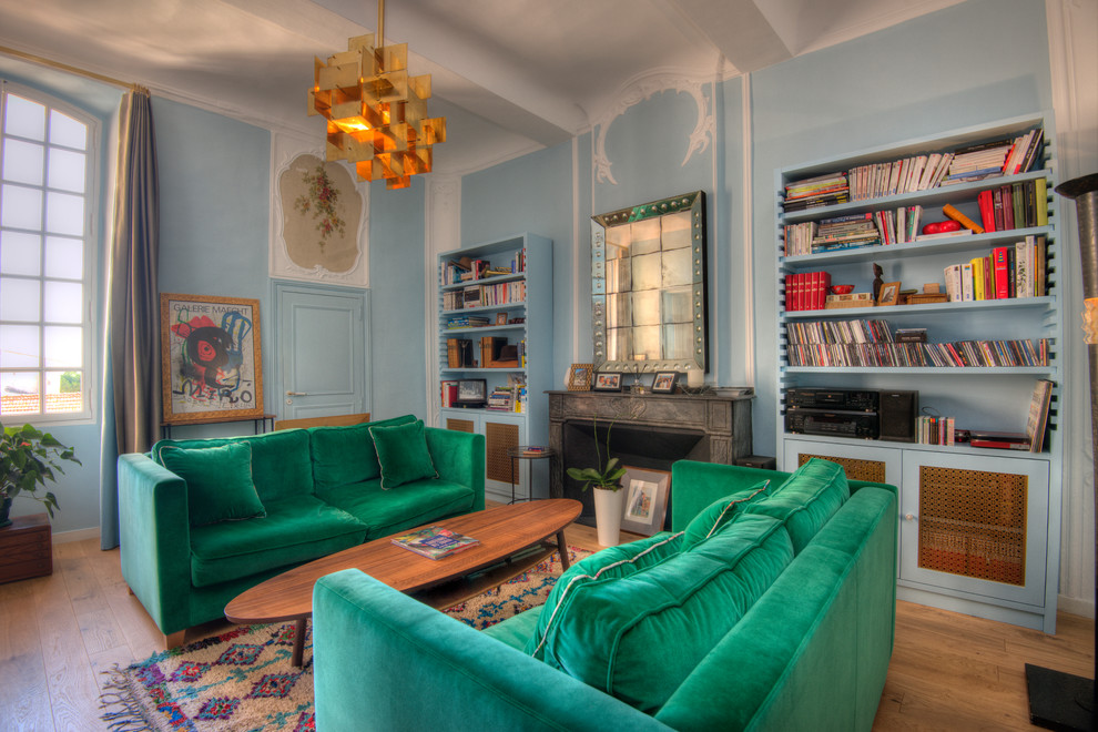 Réalisation d'un salon vintage ouvert avec une bibliothèque ou un coin lecture, un mur bleu, parquet clair, une cheminée standard, un manteau de cheminée en pierre et aucun téléviseur.