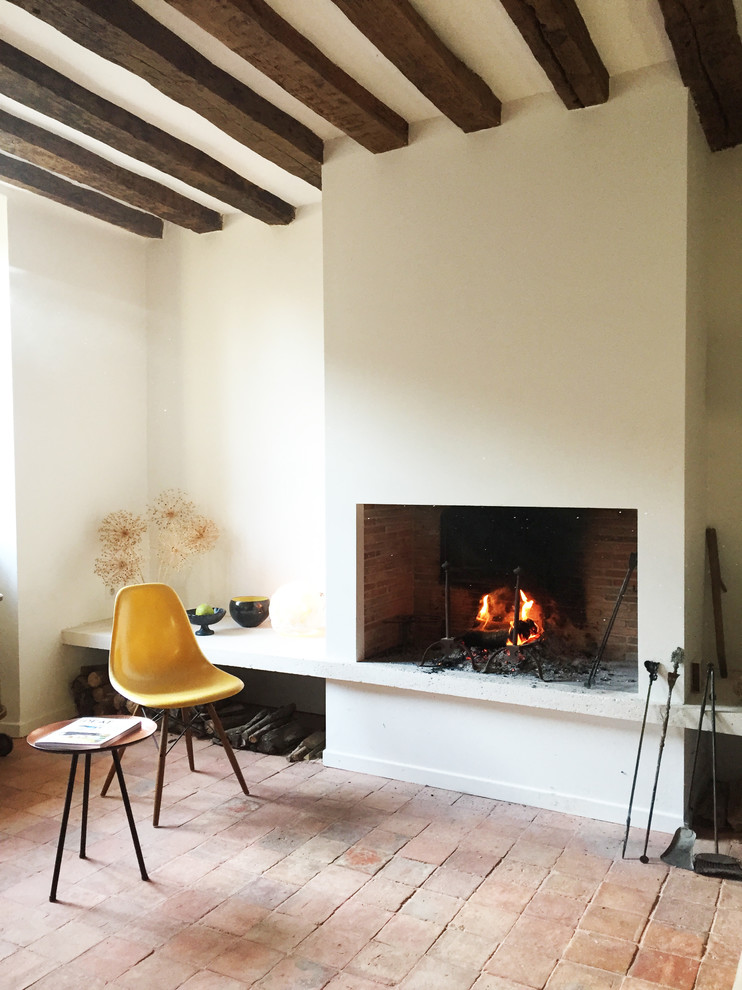 Exemple d'un salon nature de taille moyenne et ouvert avec un mur beige, tomettes au sol, une cheminée standard, un manteau de cheminée en plâtre et aucun téléviseur.