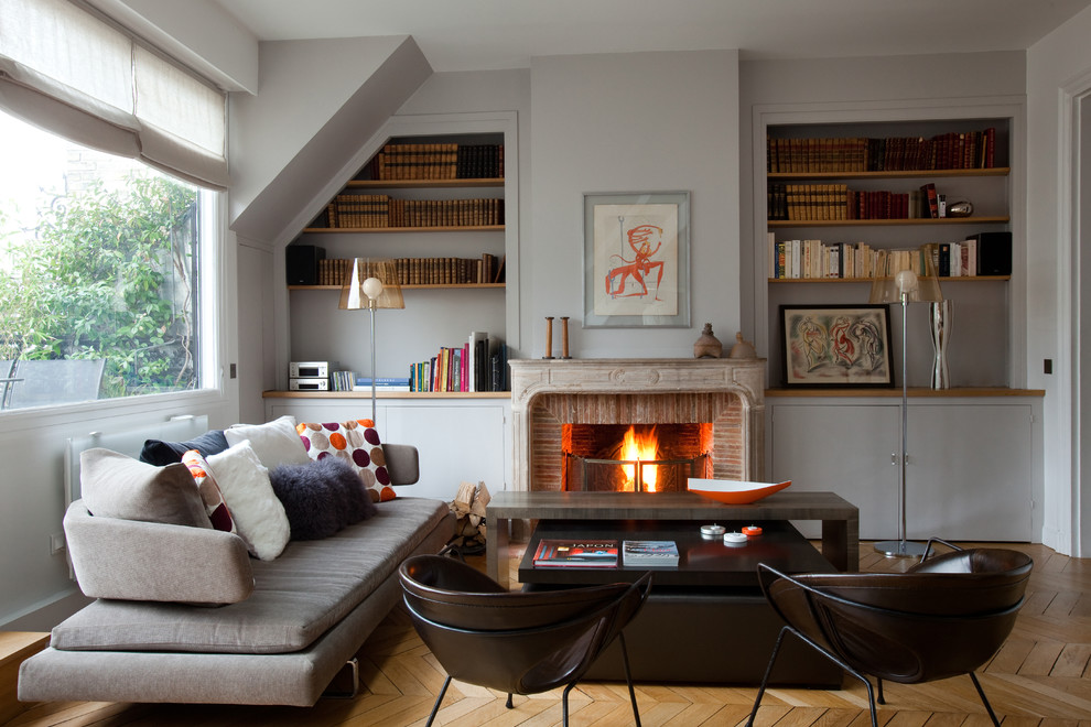 Idée de décoration pour un salon champêtre de taille moyenne et fermé avec un mur gris, parquet clair, une cheminée standard, un manteau de cheminée en brique, une bibliothèque ou un coin lecture et aucun téléviseur.