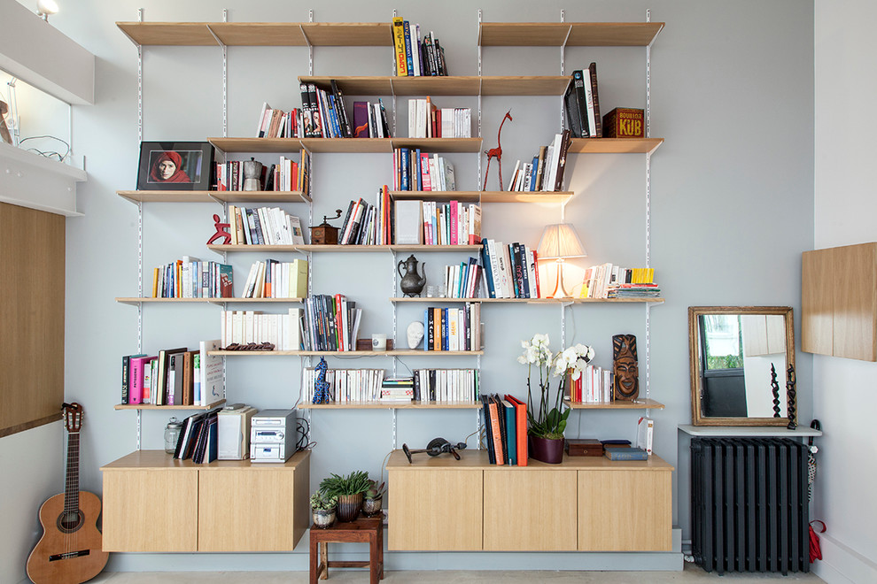 На фото: открытая гостиная комната в стиле фьюжн с серыми стенами, бетонным полом и с книжными шкафами и полками без телевизора