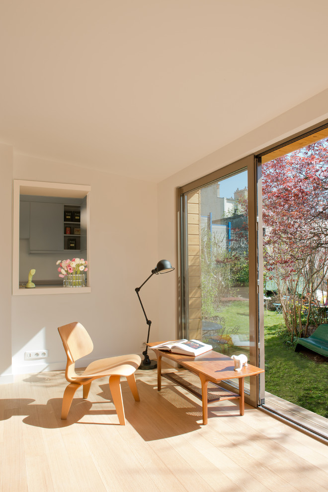 На фото: открытая гостиная комната среднего размера в скандинавском стиле с белыми стенами, светлым паркетным полом и с книжными шкафами и полками без камина, телевизора