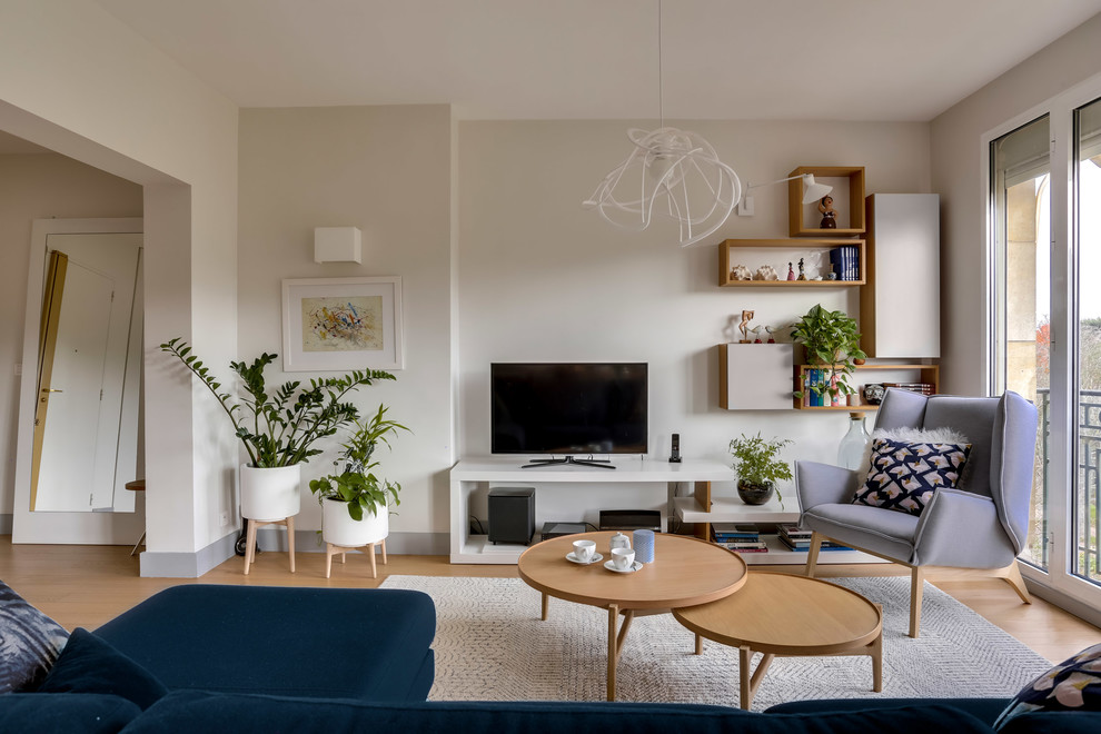На фото: открытая гостиная комната в скандинавском стиле с белыми стенами, паркетным полом среднего тона, отдельно стоящим телевизором и коричневым полом