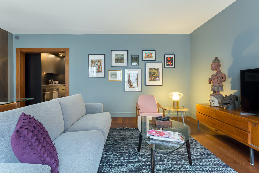 Exemple d'un salon tendance ouvert avec un mur bleu, un sol en bois brun, aucune cheminée, un téléviseur indépendant, un sol marron et éclairage.